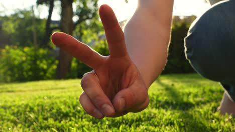 Nahaufnahme-Einer-Person,-Die-Bei-Sonnenuntergang-Mit-Den-Fingern-Ein-Friedenszeichen-Vor-Gartenhintergrund-Macht