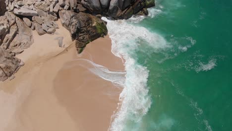 Birdseye-View-of-Waves-Crashing-onto-Shore-Alongside-Rocks
