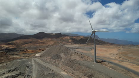 Single-wind-turbine-rotating-on-dusty-desert-mountain-range-landscape-aerial-view-orbit-left