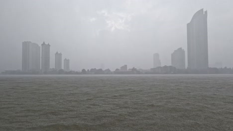 Heavy-rain-or-rainstorm-over-Chao-Phraya-River-in-Bangkok-with-high-buildings-silhouette-in-background,-Thailand