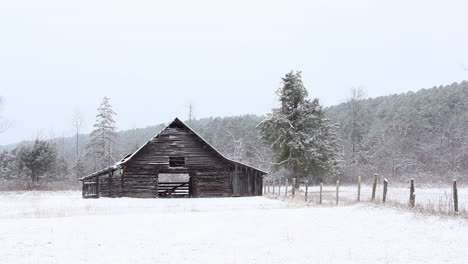 A-light-snowfall-in-front-of-a-weathered-old-wooden-barn-in-a-snow-covered-pasture-in-rural-Arkansas