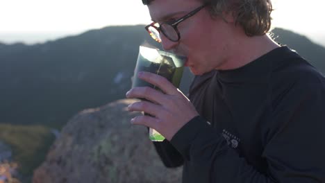 Young-hiker-on-evening-mtn-summit-enjoys-steaming-hot-mug-of-tea