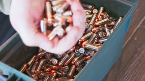 Close-up-view-of-someone-opening-up-a-can-of-9mm-ammunition,-pulling-out-a-handful-of-loaded-bullets,-shaking-it-in-their-hand-and-then-pulling-it-away