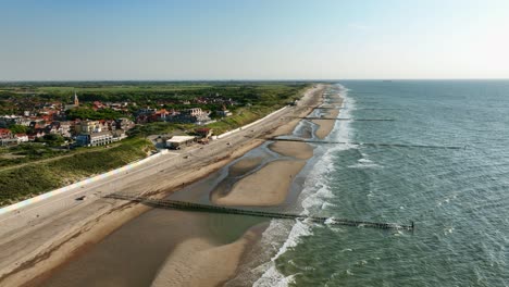 Beautiful-aerial-shot-of-a-beach-in-a-rural-area,-with-wooden-groins-to-prevent-erosion,-on-a-cloudless-summer-day