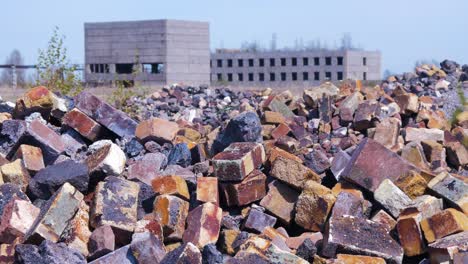 Exterior-view-of-abandoned-Soviet-heavy-metallurgy-melting-factory-Liepajas-Metalurgs-territory,-piles-of-debris-and-old-bricks,-distant-brick-buildings,-sunny-day,-medium-shot