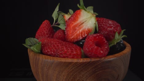 Unglaublich-Saftige-Rotierende-Waldfrüchte-In-Einer-Holzschale-Mit-Schwarzem-Hintergrund,-Erdbeeren,-Blaubeeren,-Himbeeren,-Gesunde-Früchte,-4K-Aufnahme