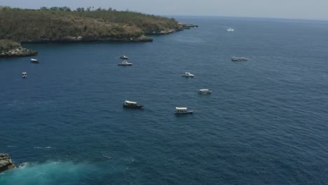 snorkeling-tour-boats-anchored-in-the-blue-ocean-around-crystal-bay-in-nusa-penida-bali-on-a-sunny-day,-aerial