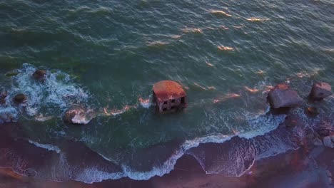 Aerial-birdseye-view-of-abandoned-seaside-fortification-buildings-at-Karosta-Northern-Forts-on-the-beach-of-Baltic-sea-,-waves-splash,-golden-hour-sunset,-static-drone-shot