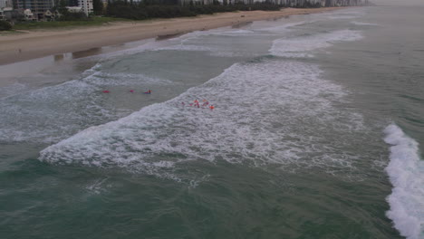 Aerial-view-of-a-group-of-Nippers-running-into-the-water-during-a-morning-training-session-with-water-safety-watching-on-at-Mermaid-Beach-Gold-Coast-QLD-Australia