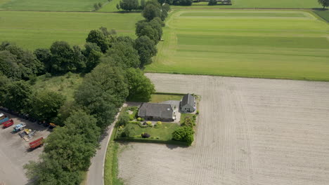 Aerial-of-small-farm-house-near-a-harvested-pasture-surrounded-by-green-meadows