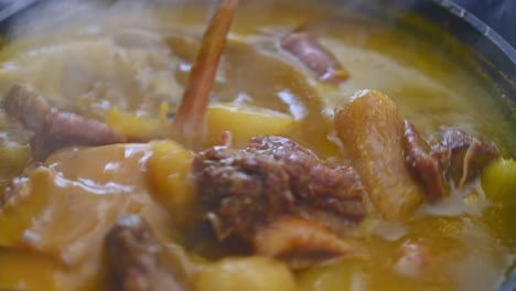 Handheld-close-up-view-of-wooden-ladle-showing-meat-of-steaming-traditional-Dominican-creole-food-called-Sancocho