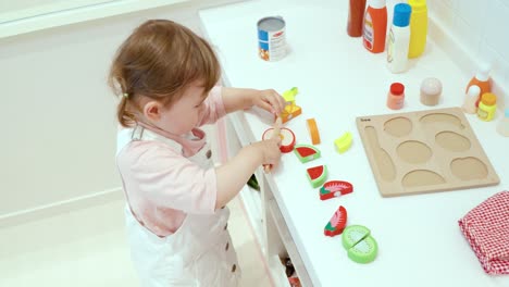 Female-Toddler-Playing-With-Fruits-Cutting-Play-Toy-Set-At-The-Playroom-Of-A-Child-friendly-Cafeteria