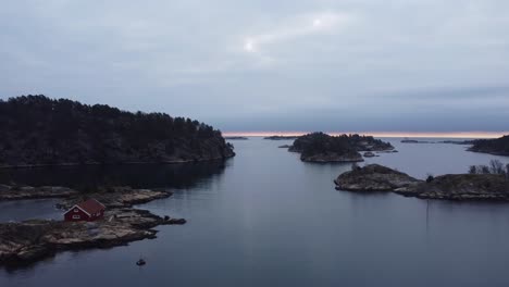Evening-aerial---Flying-above-ocean-surface-in-Lillesand-Norway-towards-horizon-and-North-sea---Cloudy-sky-and-dark-coastal-islands-Risholmen-and-Hoyholmen-and-Tjuvholmen