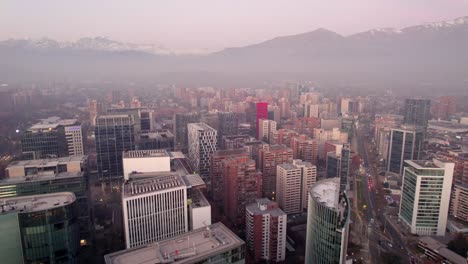 Vista-Aérea-Panorámica-Izquierda-De-Los-Edificios-Del-Municipio-De-Las-Condes,-Con-La-Cordillera-Al-Fondo-En-Una-Tarde-De-Smog,-Santiago,-Chile.
