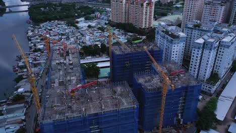 Drohnen-Umlaufbahn-Eines-Großen-Modernen-Wohnbauprojekts-In-Südostasien,-Das-Entlang-Eines-Kanals-Mit-Ursprünglichen-Flachhäusern-Und-Zersiedelung-Gebaut-Wird