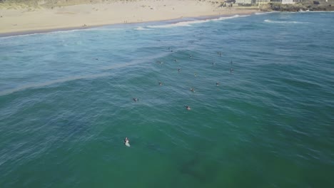 Aerial-drone-shot-flying-over-surfers-on-the-waves-of-the-atlantic-ocean,-at-sunset,-in-praia-do-Guincho,-on-a-sunny-evening,-at-the-coast-of-Cascais,-in-Portugal