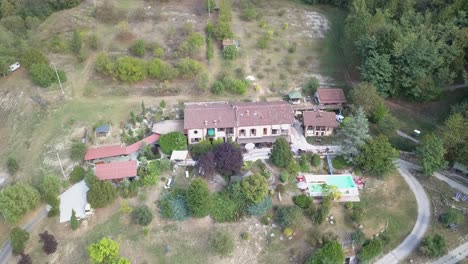 Big-vacation-house-with-a-pool-and-a-road-on-a-hilly-forest,-drone-aerial-view-in-the-italian-countryside
