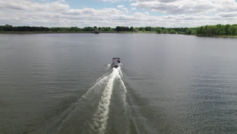 Aerial-drone-shot-over-white-motor-boat-speeding-over-lake-water-on-a-cloudy-day