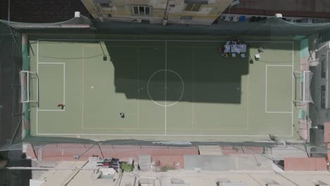 Overhead-aerial-footage-of-kids-playing-soccer-in-a-field-surrounded-by-buildings-in-Naples,-Italy