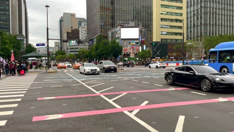Slow-motion-shot-of-many-cars-on-frequented-junction-in-Seoul-and-pedestrian-crossing-road-during-daytime