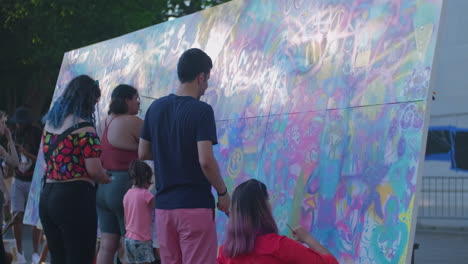 Medium-shot-of-multicultural-group-of-people-painting-a-big-canvas-in-a-public-park