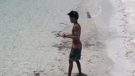 Un-Joven-Trabajador-Tirando-Hilo-De-Pescar-En-La-Playa,-Pescando-En-La-Costa-Arenosa-En-Un-Día-Soleado