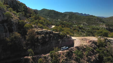 White-car-driving-up-arid-mountain-road-in-Copper-Canyon,-Mexico,-forward-aerial