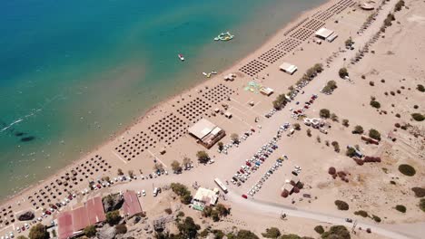 Goldene-Sandküste-Mit-Nipa-Sonnenschirmen-Und-Geparkten-Fahrzeugen-Im-Sommer-Am-Strand-Von-Tsambika,-Insel-Rhodos,-Griechenland