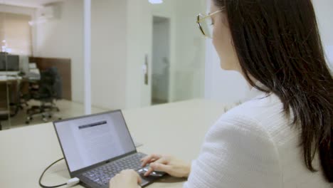 Una-Mujer-Que-Trabaja-En-Una-Oficina-De-Negocios-Con-Una-Computadora-Portátil-En-Un-Escritorio,-Escribiendo-Un-Documento
