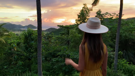 Young-Women-In-Yellow-Dress-Wearing-Hat-Seeing-Golden-Sunset-Through-Jungle-Trees-In-Lombok,-Indonesia