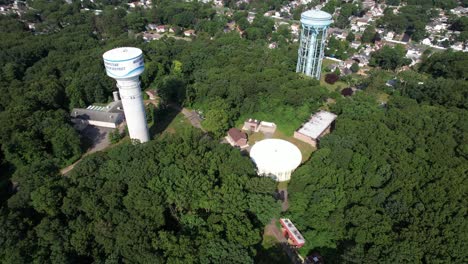 A-top-down-drone-view-over-a-golf-course,-then-tilt-up-to-reveal-water-towers-in-a-suburban-neighborhood-on-Long-Island,-NY-on-a-sunny-day