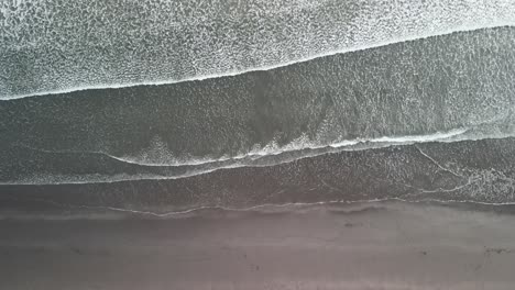 Steady-tripod-drone-shot-of-waves-on-black-sand-beach