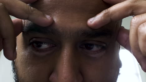 Eine-Extreme-Nahaufnahme-Des-Gesichts-Eines-Asiatischen-Indischen-Mannes,-Der-Sich-Mit-Den-Fingerspitzen-Die-Stirn-Massiert,-Während-Seine-Augen-Fokussiert-Bleiben