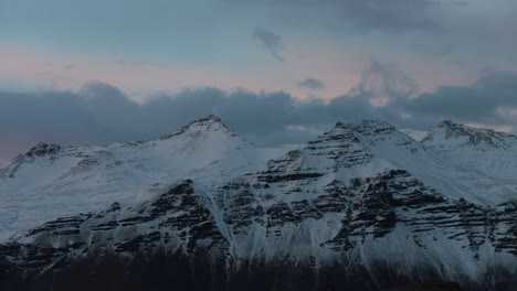 Clouds-over-snow-covered-mounain-peaks-illluminated-at-dusk,-telephoto-time-lapse