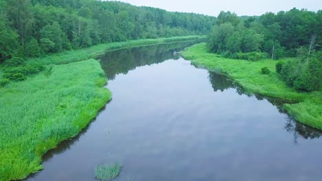 Aerial-view-of-a-Venta-river-on-a-sunny-summer-day,-lush-green-trees-and-meadows,-beautiful-rural-landscape,-wide-angle-drone-shot-moving-backward