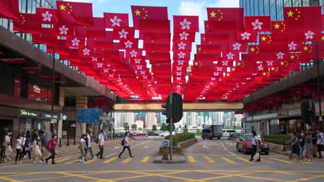 Menschen-überqueren-Die-Straße,-Während-In-Hongkong-Flaggen-Der-Volksrepublik-China-Und-Der-SAR-Hongkong-Vor-Dem-1.-Juli,-Dem-Jahrestag-Der-Übergabe-Hongkongs-An-China,-Gezeigt-Werden