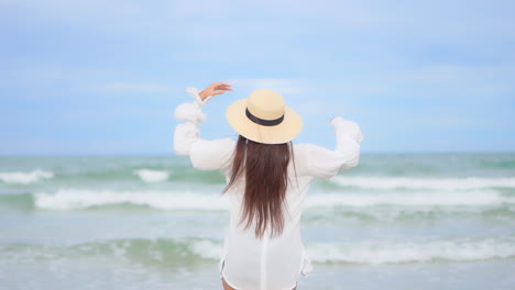 Woman-in-White-Blouse-Standing-on-the-Beach-by-the-Sea-and-Raising-Arms-up-Facing-Endless-Seascape---vacation-template-back-view