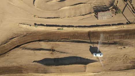 Ascending-over-a-motocross-racetrack-as-a-water-tank-prepares-the-track-for-the-race---straight-down-aerial-view