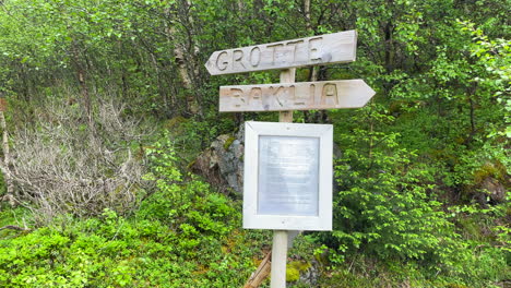 Panning-shot-of-a-sign,-showing-the-way-to-a-cave-in-Norway-during-summer