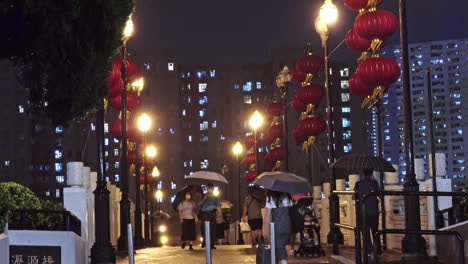 People-walk-with-umbrellas-on-Chinese-Bridge-with-Lanterns-in-Shatin,-Hong-Kong