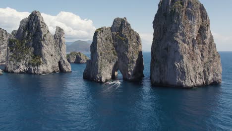 Aerial-of-Yachts-Boating-Under-the-Natural-Arch-of-the-Faraglioni-Sea-Stacks-on-Coast-of-Capri-Island,-Italy