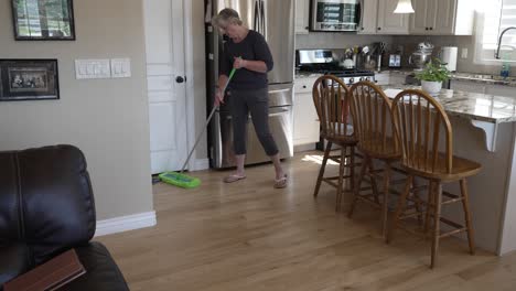 Senior-woman-dusting-and-sweeping-hardwood-oak-floors-in-the-kitchen---tilt-down