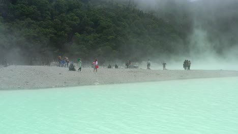 people-on-a-beach-in-a-volcano-crater-surrounded-by-a-sulfur-lake-in-Kawah-Putih,-aerial