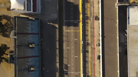 Aerial-top-down-shot-of-racing-cars-crossing-finish-line-of-racetrack-beside-stands-during-sunset---slow-motion