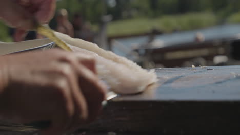 Man-cutting-fish-fillets-with-knife-on-wooden-cutting-board-outdoors-in-nature,-slow-motion