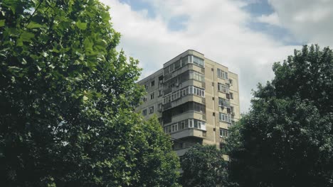 Pan-right-shot-with-a-block-of-flats-framed-by-trees-with-green-leaves,-somewhere-in-Eastern-Europe