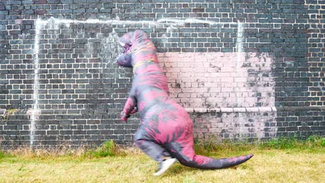 Funny-prehistoric-dinosaur-costume-hopping-and-dancing-against-brick-wall