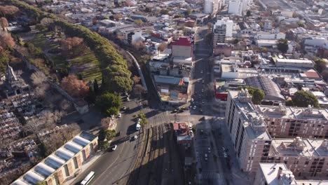 Aerial-tilt-down-shot-of-traffic-on-road-and-train-on-rail-near-Chacarita-Station-and-Cemetery-in-Buenos-Aires