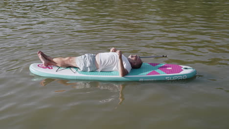 Tired-man-lying-on-paddleboard-and-resting-after-sport-activity,-clear-background,-pond-or-lake