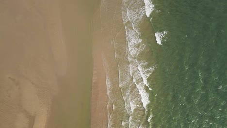 Aerial-top-down:-Waves-of-crystal-clear-ocean-reaching-sandy-beach-during-sunlight